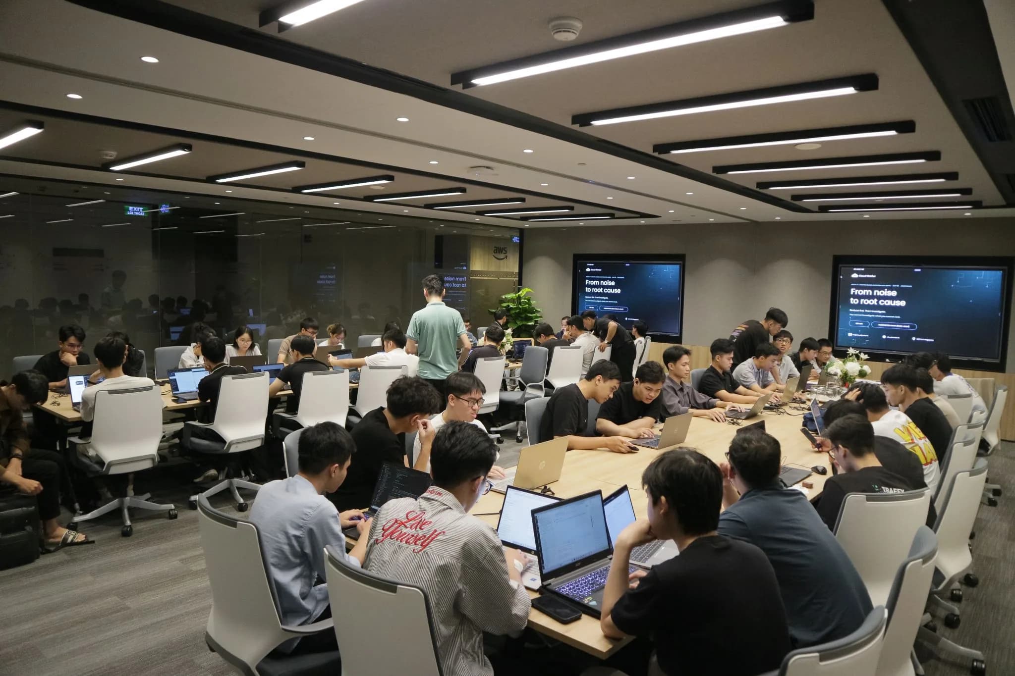A room of engineers working hands-on at laptops, with the session slides on two screens